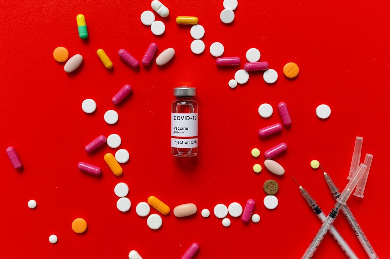 Colorful tablets and COVID-19 vaccine vial on a red background with syringes, symbolizing healthcare.